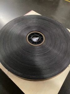 An image depicting a roll of PE tape reinforced with glass fibers, showcasing a cardboard core positioned at the center with a black plastic plug inserted for protection.